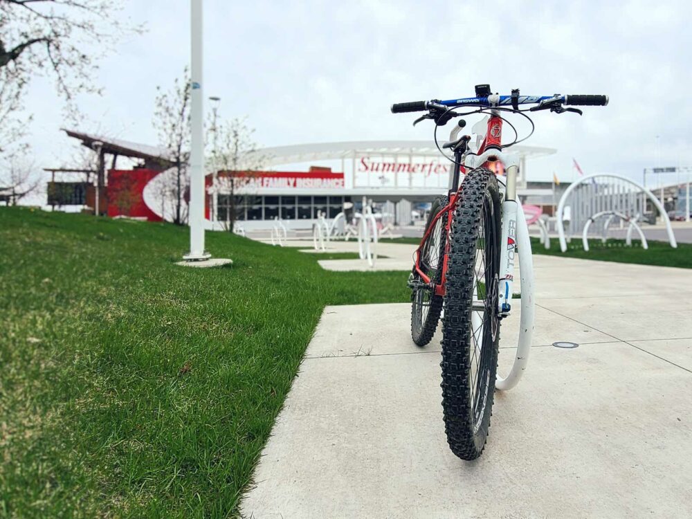 A mountain bike parked against a bike rack in front of the festival grounds